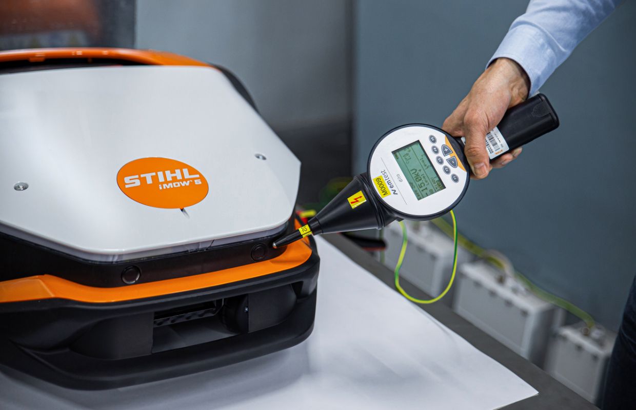 A man holds a measuring device to a robotic lawnmower (iMOW).