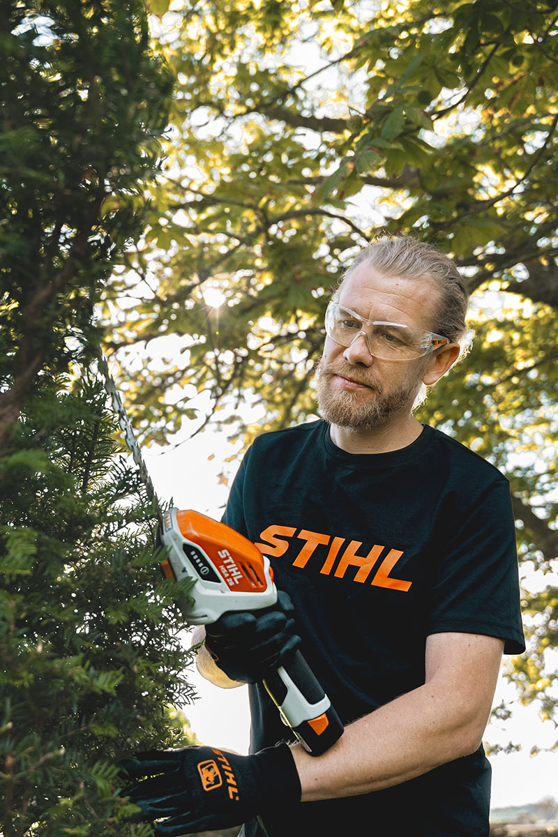 Andy Wain cuts a yew tree into shape with a cordless hedge trimmer.