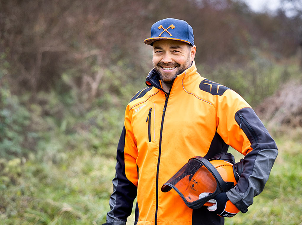 Simon Haug stands laughing in front of a green thicket.
