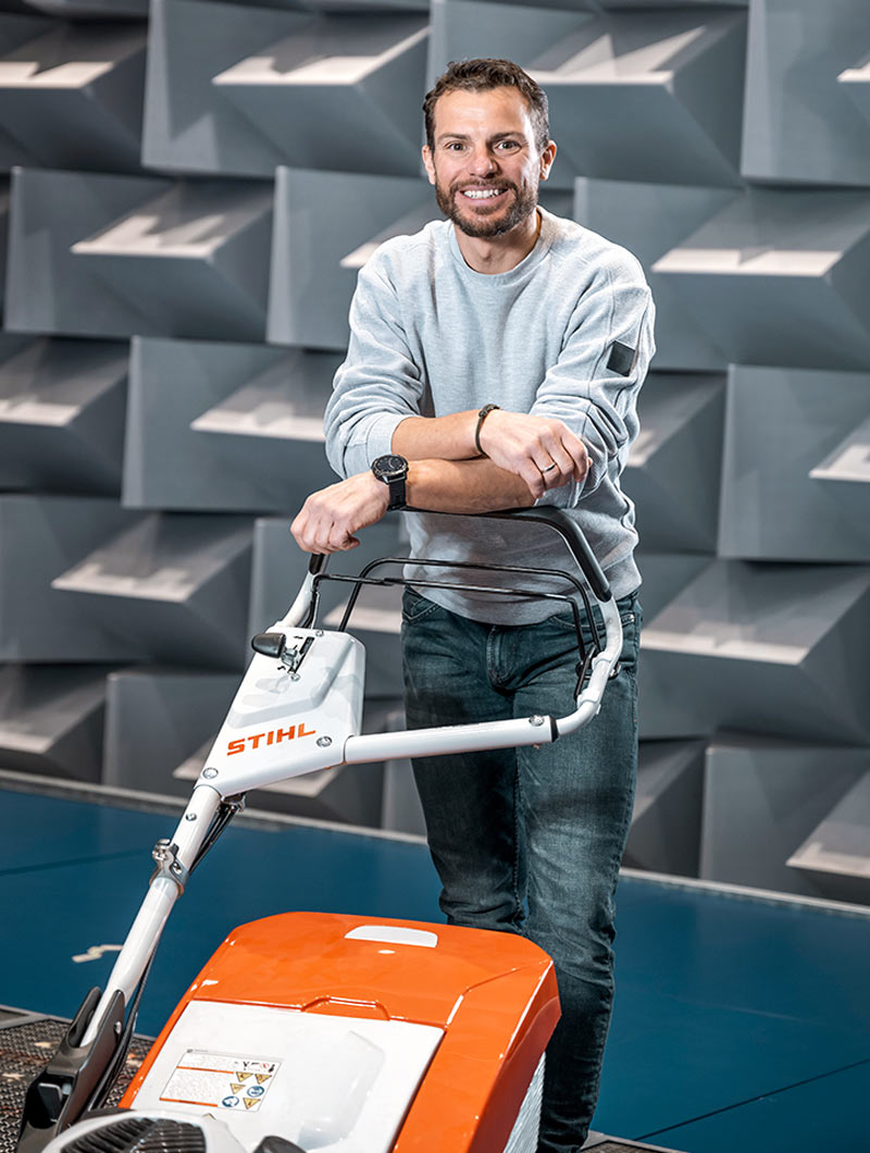 Bernhard Huber stands laughing in the anechoic chamber, leaning on a lawnmower.