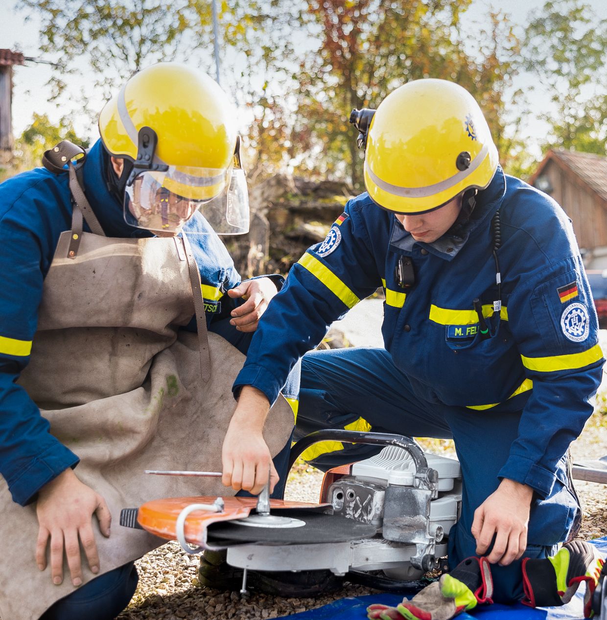 Two men in THW uniforms prepare a cut-off machine for the upcoming exercise.